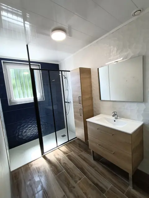 Douche à paroi vitrée noire et faïence bleu nuit en relief, meuble vasque et colonne en bois, armoire de toilette à miroir
