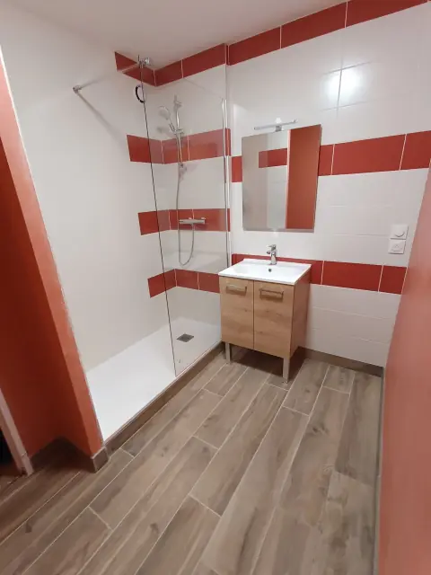 Salle d’eau avec douche vitrée, faïence blanche à bandes rouges et meuble vasque en bois