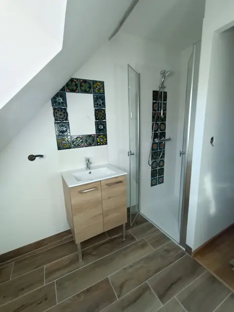 Salle d’eau sous pente avec cadre de faïence décorative, meuble vasque en bois et douche à portes pliantes